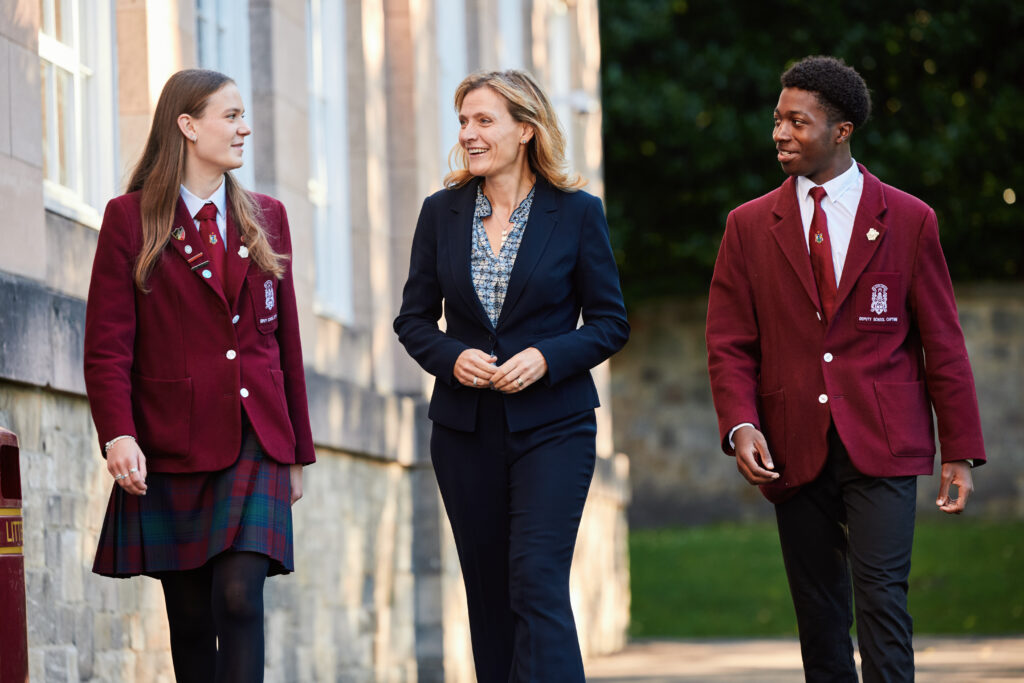 Blonde woman in suit pictured with two pupils in red blazers
